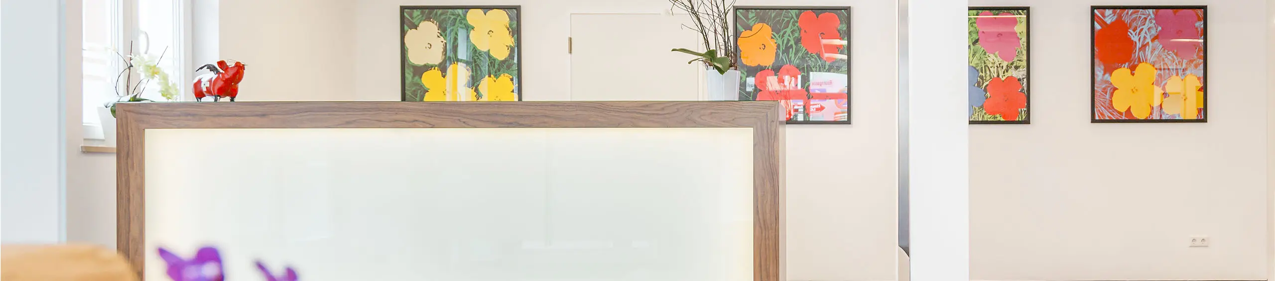 Empfangstresen mit Blumendekoration und vier bunten Blumenbildern an der Wand