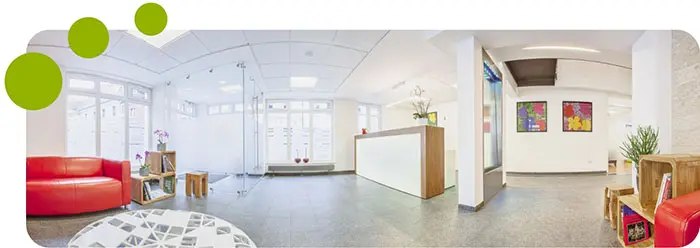 Heller, moderner Empfangsbereich mit rotem Sofa, weißem Tresen und bunten Bildern an der Wand