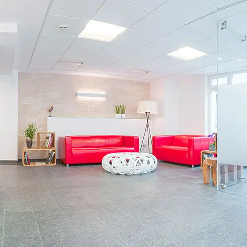 Helle Empfangshalle mit zwei roten Sofas, rundem weißen Hocker und Glastür