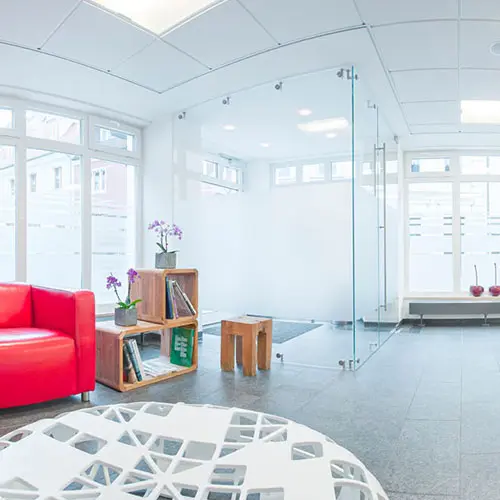 Heller Empfangsbereich mit rotem Sofa, Glastür, weißem Empfangstresen und moderner Einrichtung