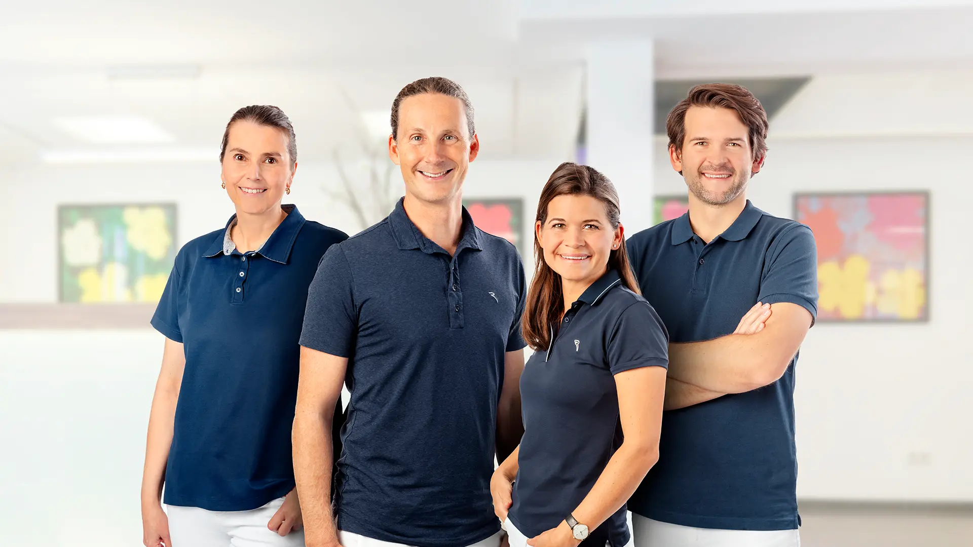 Vier Personen in dunkelblauen Poloshirts stehen nebeneinander in einem hellen Raum mit moderner Kunst an den Wänden